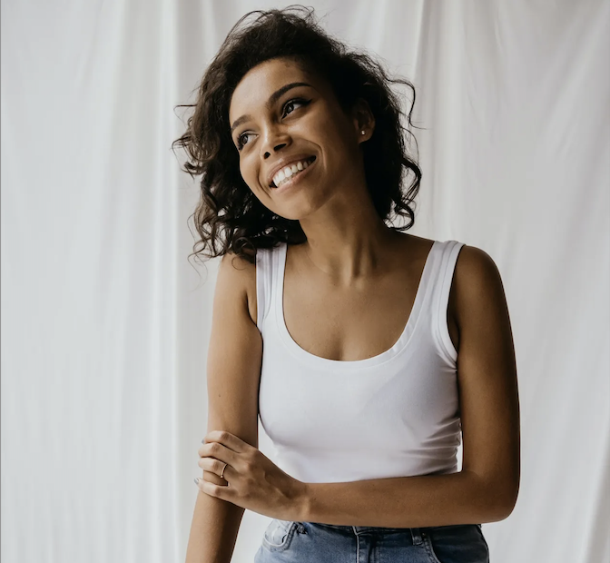 A young woman practicing gratitude while wearing a white tank top and jeans.