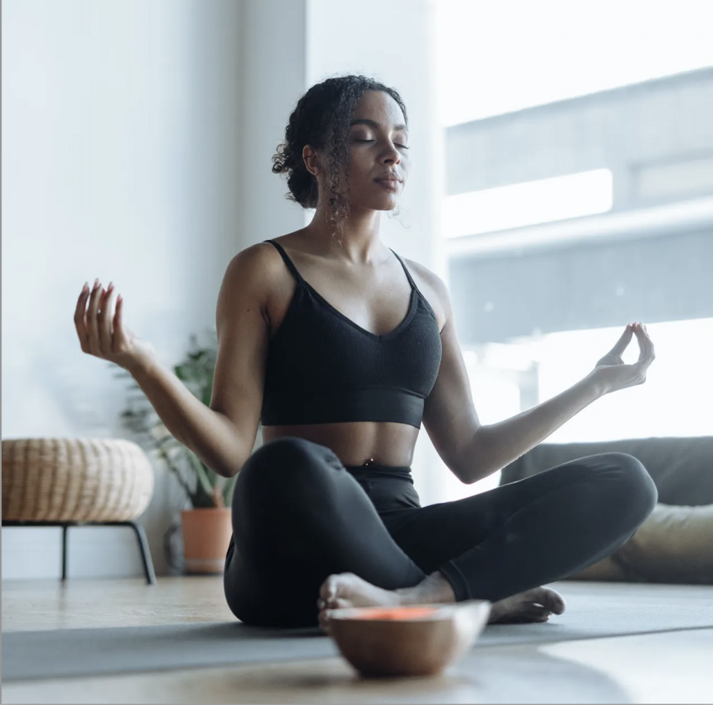 A woman practicing mindfulness in her everyday life by meditating in front of a window.