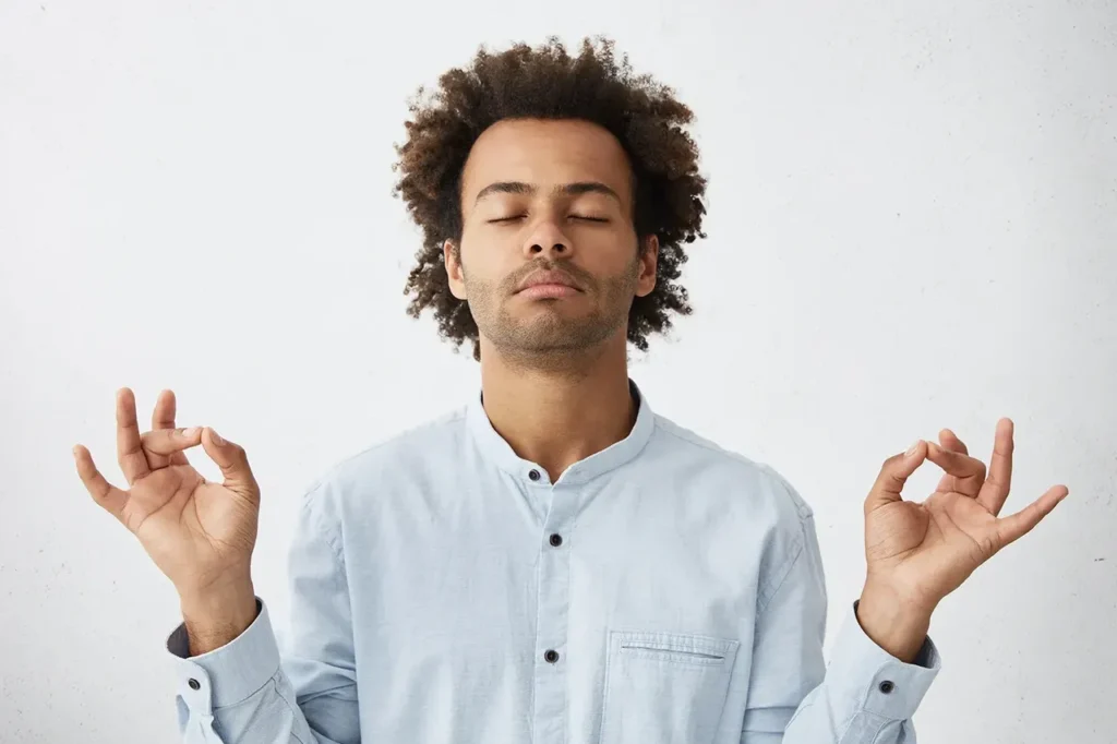 A young man practicing natural stress relief techniques while meditating on a white background.