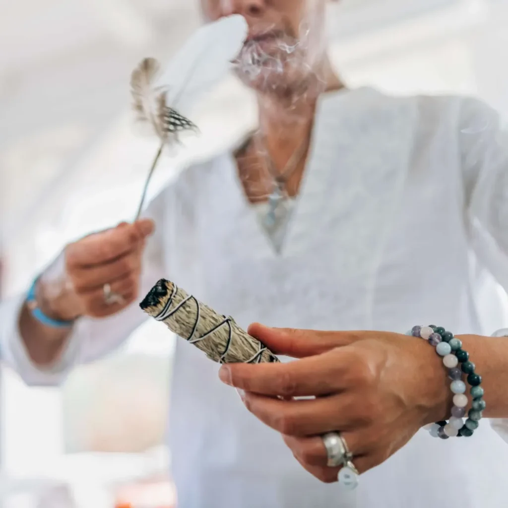 A woman holding a feather and a stick of incense, guiding the smudging ritual for its benefits.