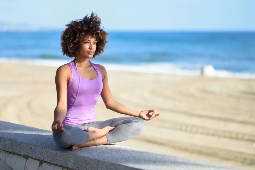 Young woman cultivating mind and health through meditation on the beach.