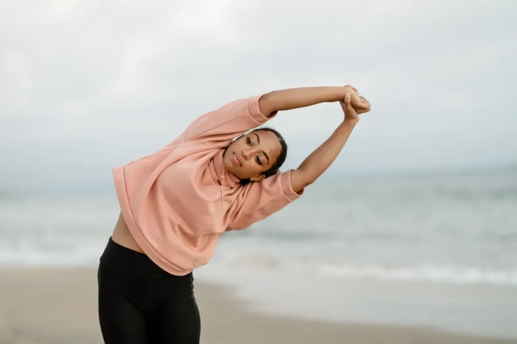 A woman moving gracefully, practicing yoga on the beach as a way to manage stress.