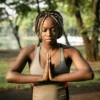 A young black woman meditating in a park to decrease her resting heart rate.