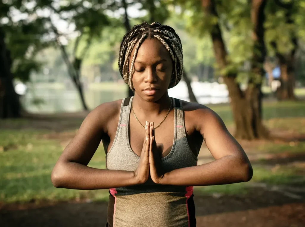 A young black woman meditating in a park to decrease her resting heart rate.