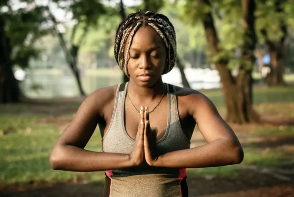 A young black woman meditating in a park to decrease her resting heart rate.