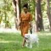 A woman engaging in self-care as she walks her white dog in a park.