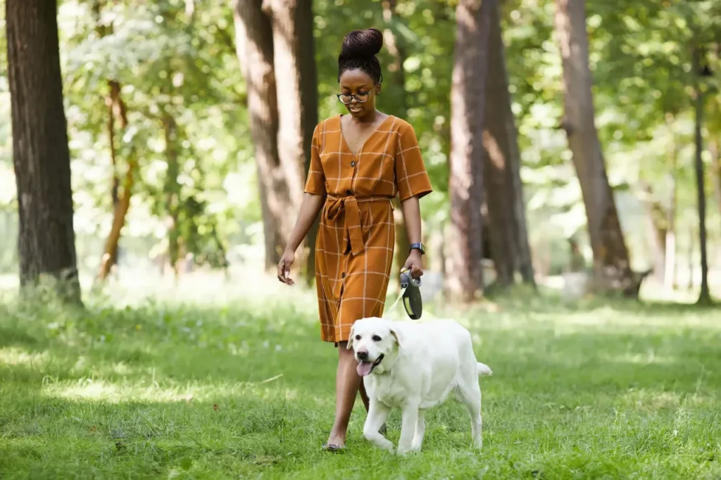 A woman engaging in self-care as she walks her white dog in a park.