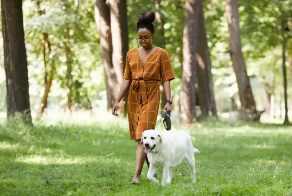 A woman engaging in self-care as she walks her white dog in a park.