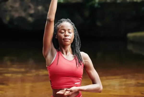 A woman in red practices mindful breathing while doing yoga in a river.