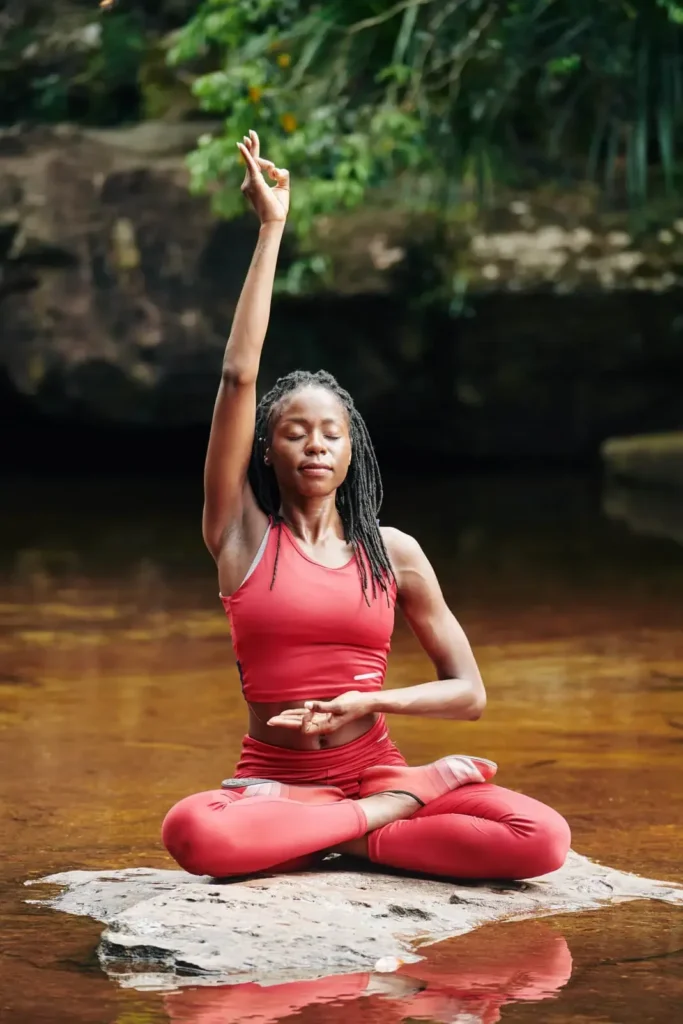 A woman in red practices mindful breathing while doing yoga in a river.