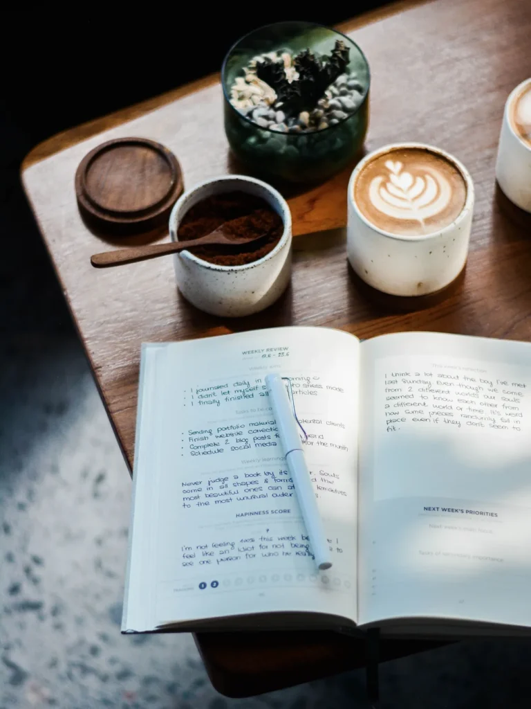 A mindfulness journal, accompanied by coffee cups and a pen, resting on a rustic wooden table.