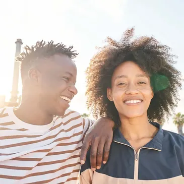 A young couple, smiling at each other, on the beach; a heartwarming scene.