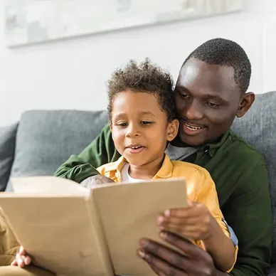 About Us: A father and son sitting on the couch, engrossed in reading a book together.