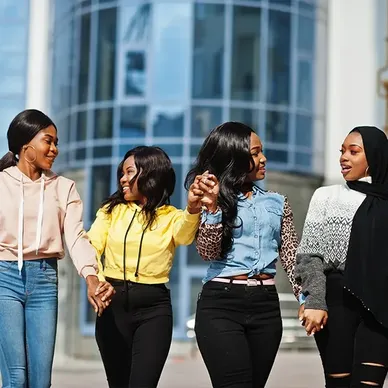 About Us: A group of young women SYM hands walking down a city street.