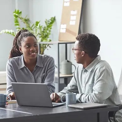 About Us: Two business people sitting at a table in an office, discussing SYM.