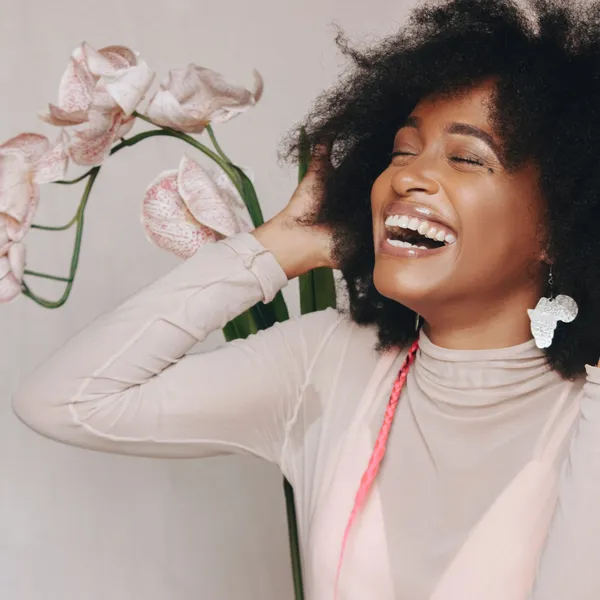 About Us: A woman with afro hair laughing in front of a flower.