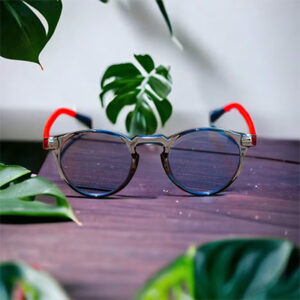 A pair of Blue Light Blocking Photochromic Glasses Round Circle Lenses - Grey/ Red/Blue sitting on a table next to a plant.