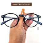 A person holding up a pair of Blue Light Blocking Photochromic Glasses Round Circle Lenses - Black & Blue glasses with the words free case included.