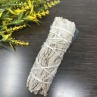 California Organic White Sage Smudge Sticks, commonly found in California, are a popular organic herb used for smudging rituals. In this scenario, a California Organic White Sage Smudge Stick is placed delicately on a wooden table to create.