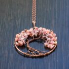 A Rhodochrosite Tree of Life pendant on a wooden table.