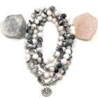 A unique Pink Zebra Stone 108 Mala Gemstone Bead Necklace featuring a lotus stone and a lotus charm, adorned with a mesmerizing Pink Zebra Stone.