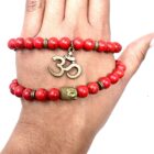 A hand holding a Red Howlite Gemstone Bead Double Om Charm Bracelet with an om symbol on it, made of Red Howlite Gemstone.