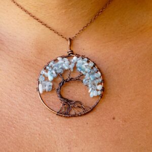 A woman is wearing an Aquamarine Tree of Life pendant necklace.