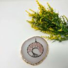 A pink rose quartz Tree of Life pendant on a gold plate.