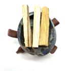 Four Palo Santo sticks - Thick in a bowl on top of a white surface, emitting a soothing home fragrance.