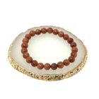 A Red Goldstone Gemstone bracelet with red jade beads on a gold plate.