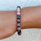 A woman's wrist adorned with a beautiful Matrix Rhodonite Gemstone Bracelet featuring a rhodonite stone set against a striking black matrix.