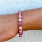 A Pink Rhodonite Gemstone Bracelet 8mm on a woman's wrist.