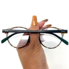 A hand holding a pair of Blue Light Blocking Photochromic Glasses with round circle lenses in a tortoise pattern.