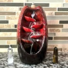 A red ceramic Red Ceramic Waterfall Backflow Incense Burner with Mixed Incense Cones sitting on a counter.