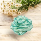 A teal flower with white daisies on top of a wooden table. The green leaves enhance the vibrant colors of the Rose Loofah - Green.