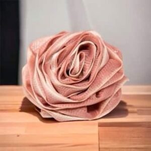 A Rose Loofah- Dark Pink & White is sitting on a wooden table.