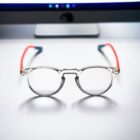 A pair of Blue Light Blocking Photochromic Glasses Round Circle Lenses - Grey/ Red/Blue on a desk next to a computer.