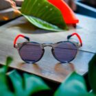 A pair of Blue Light Blocking Photochromic Glasses Round Circle Lenses - Grey/ Red/Blue sitting on top of a wooden table.