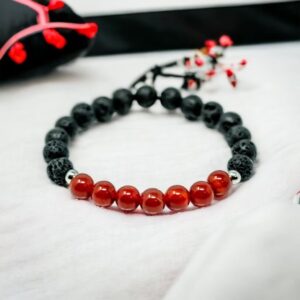 A black and red Gemstone Crystal Bracelet, Carnelian, Lava, Stainless Steel 6mm with carnelian gemstone crystals on a bed.