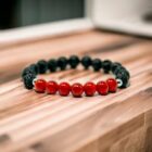 A Gemstone Crystal Bracelet, Carnelian, Lava, Stainless Steel 6mm with red carnelian and black lava beads on top of a wooden table.