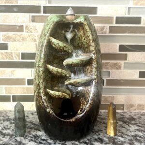 An Olive Ceramic Waterfall Backflow Incense Burner with Mixed Incense Cones sits on top of a counter.